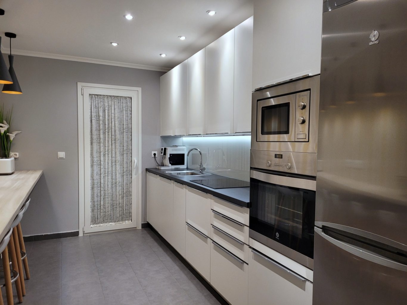 Cocina moderna con muebles blancos, electrodomésticos de acero inoxidable y luz suave.