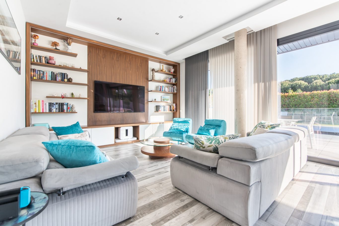 Sala de estar moderna con sofá gris, sillas turquesa y grandes ventanales.