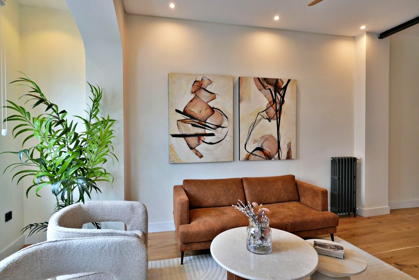 Sala moderna con un sofá marrón, arte abstracto en las paredes y planta verde.